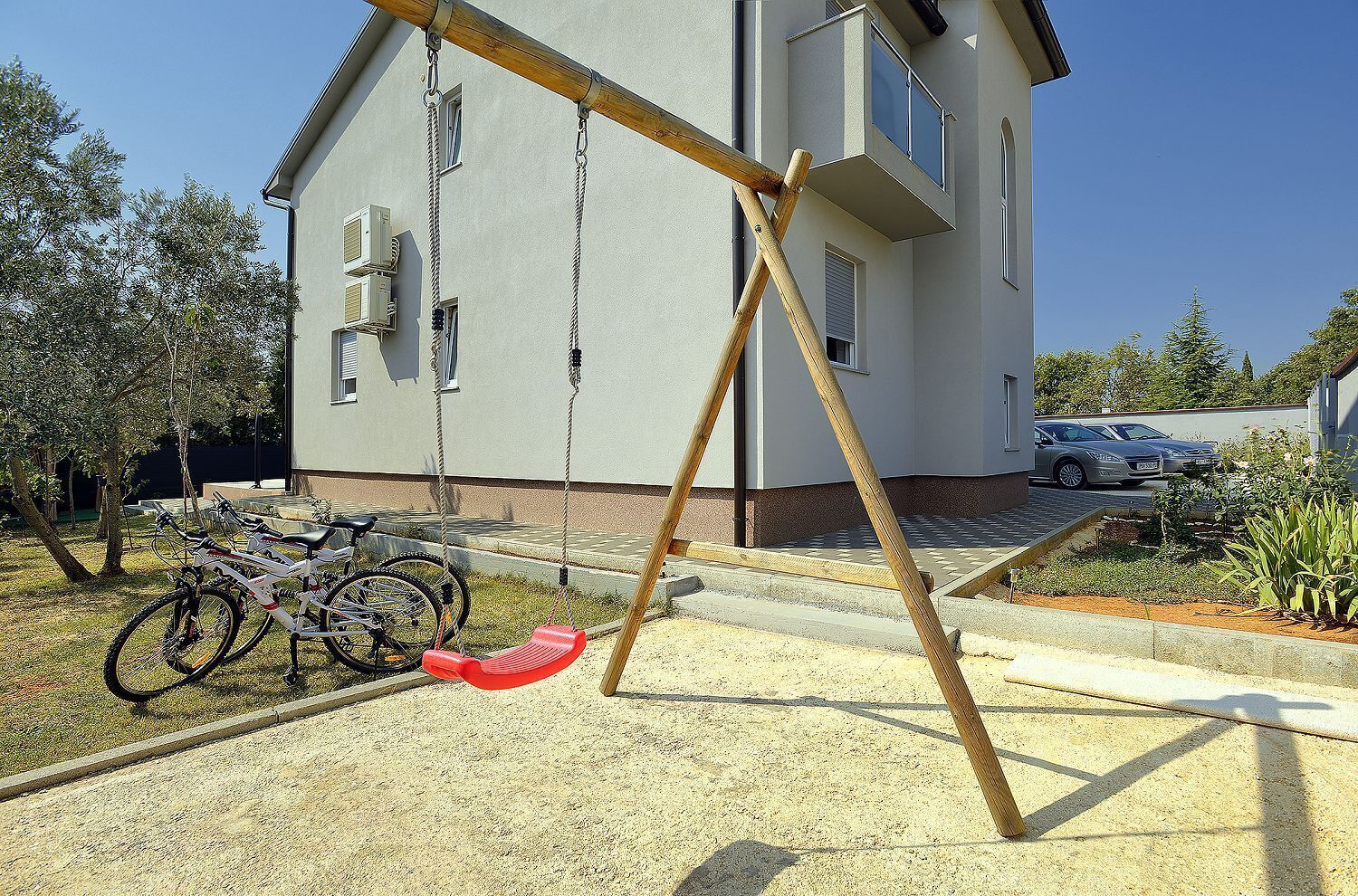 Une maison moderne avec un portique, des vélos et une voiture garée dans l’allée.