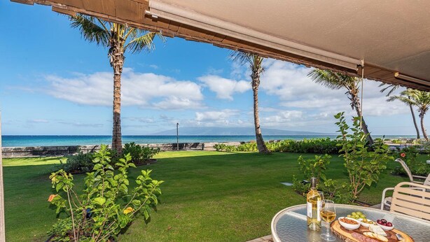 A patio with a table set for a meal, overlooking a grassy area with palm trees and a view of the ocean. - Reduced Rates! Charming Ground-Floor 1 BR, 1 BA Condo at 103 Darling with A/C (Lahaina)