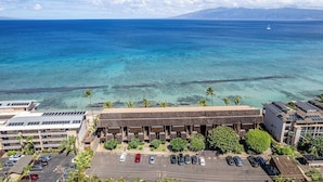A coastal hotel with a parking lot, a building with a flat roof, and a view of the ocean. - Reduced Rates! Charming Ground-Floor 1 BR, 1 BA Condo at 103 Darling with A/C (Lahaina)