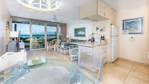 A modern kitchen with white cabinetry, a dining area with a glass table, and a view of the sea. - Reduced Rates! Charming Ground-Floor 1 BR, 1 BA Condo at 103 Darling with A/C (Lahaina)