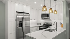 A modern kitchen with white cabinetry, stainless steel appliances, a marble countertop, and pendant lighting. - Newly Renovated Beach Front 2 bed, 2 bath at Sanibel Moorings #1121 (Sanibel)