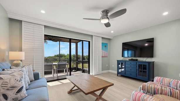 A spacious living room with a wooden coffee table, a sofa, a striped couch, a TV, and a ceiling fan. - Newly Renovated Beach Front 2 bed, 2 bath at Sanibel Moorings #1121 (Sanibel)