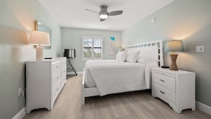 A bedroom with a bed, nightstands, a ceiling fan, and a window with blinds. - Newly Renovated Beach Front 2 bed, 2 bath at Sanibel Moorings #1121 (Sanibel)