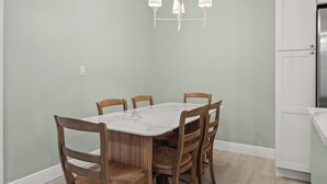 A dining area with a marble table and wooden chairs, a light green wall, and a kitchen with white cabinets. - Newly Renovated Beach Front 2 bed, 2 bath at Sanibel Moorings #1121 (Sanibel)