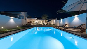 A swimming pool at night with surrounding lounge chairs and a building in the background. - Villa Licia - Villa with pool by the beach (Santa Maria del Focallo)