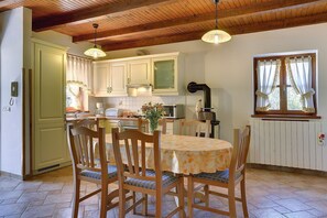 Una cucina con mobili impiallacciati in legno, un tavolo da pranzo con sedie, una lampada a sospensione e una finestra con tende.