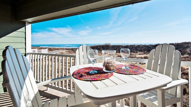 Una mesa blanca con dos sillas en un balcón con vistas a la playa.