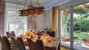 A dining area with a wooden table set for breakfast, large windows, and a view of the garden.