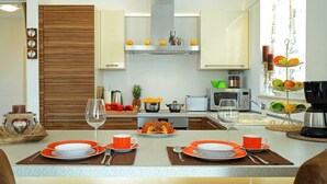 A modern kitchen with wooden cabinets, a central island with orange plates, and a fruit display.