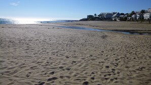 Une plage de sable avec des empreintes de pas, une mer calme et des bâtiments en arrière-plan.