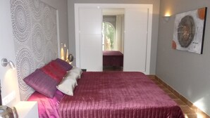 Une chambre à coucher avec un grand lit, une table de chevet, une lampe fixée au mur et une porte donnant sur une autre pièce.