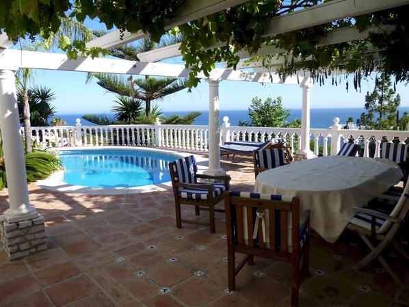 A pool area with a pergola, lounge chairs, and a table.