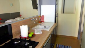 A compact kitchen with a gas stove, a sink, and a small countertop. There are apples and a roll of paper towels on the counter. - Themis (Cannes)