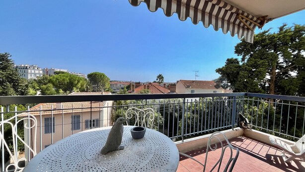 Un balcon avec une table ronde, une sculpture d’oiseau et une vue sur des immeubles et des arbres.