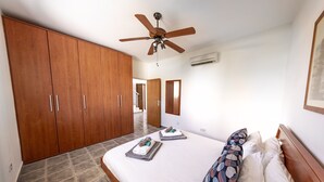 Un dormitorio con una cama grande, un ventilador de techo, un armario de madera y una escalera que lleva a otra habitación.