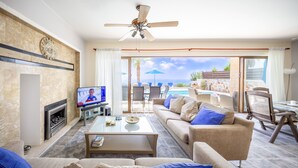 Ein Wohnzimmer mit Fernseher, Sofa, Couchtisch und Blick auf Pool und Garten.