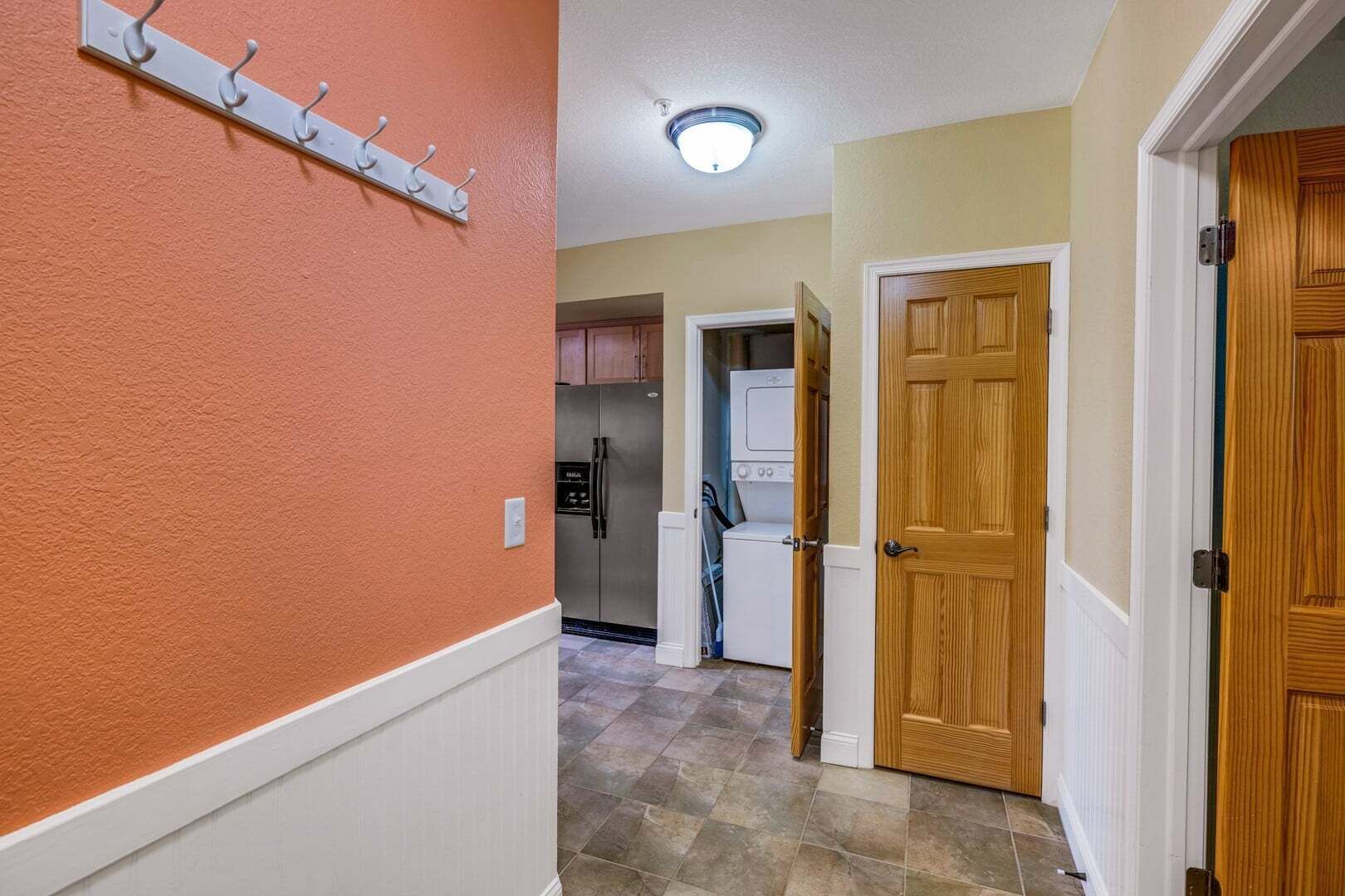 A hallway with a coat rack, a refrigerator, a washing machine, and wooden doors.
