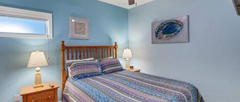 A bedroom with a wooden bed, two bedside tables with lamps, a ceiling fan, a window, and a framed picture on the wall.