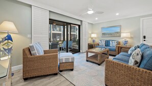 A spacious living room with wicker furniture, a glass door leading to a balcony, and a painting on the wall. - Newly Renovated Beachfront 3 bed, 2 bath at Sanibel Moorings #711 (Sanibel)
