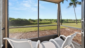 A covered outdoor seating area with a view of a grassy field and palm trees. - Newly Renovated Beachfront 3 bed, 2 bath at Sanibel Moorings #711 (Sanibel)