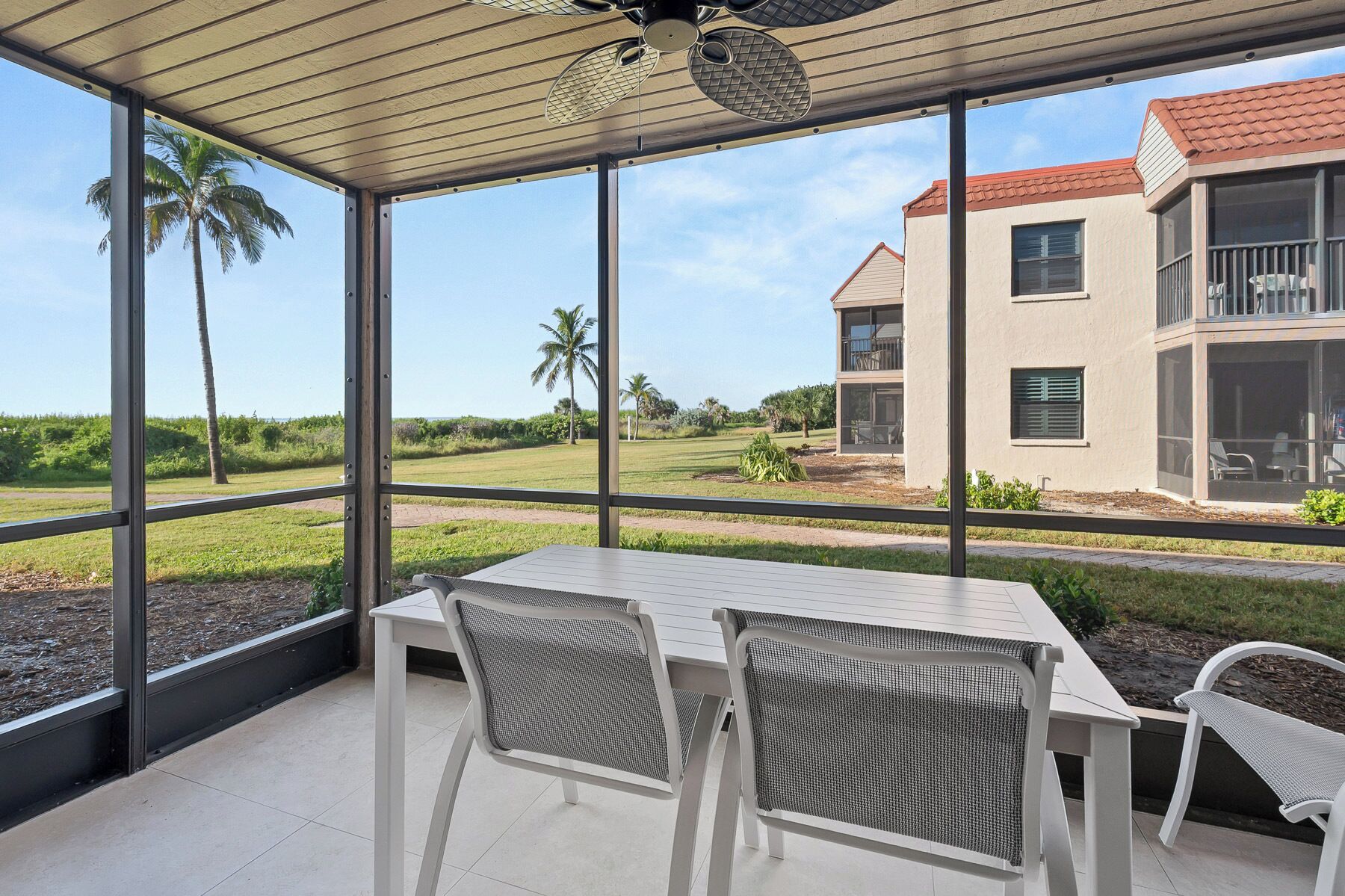 A covered patio with a table and chairs, overlooking a landscaped area and a building with balconies.