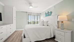 A bedroom with a bed, nightstands, a ceiling fan, and a window with blinds. - Newly Renovated Beachfront 3 bed, 2 bath at Sanibel Moorings #711 (Sanibel)