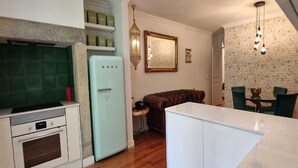 A compact kitchen with a refrigerator, oven, and a small dining area with a table and chairs. - Pateo Boaventura in Bairro Alto (Lisbon)