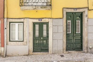 A building facade with two green doors, a window, and a number '91' sign.