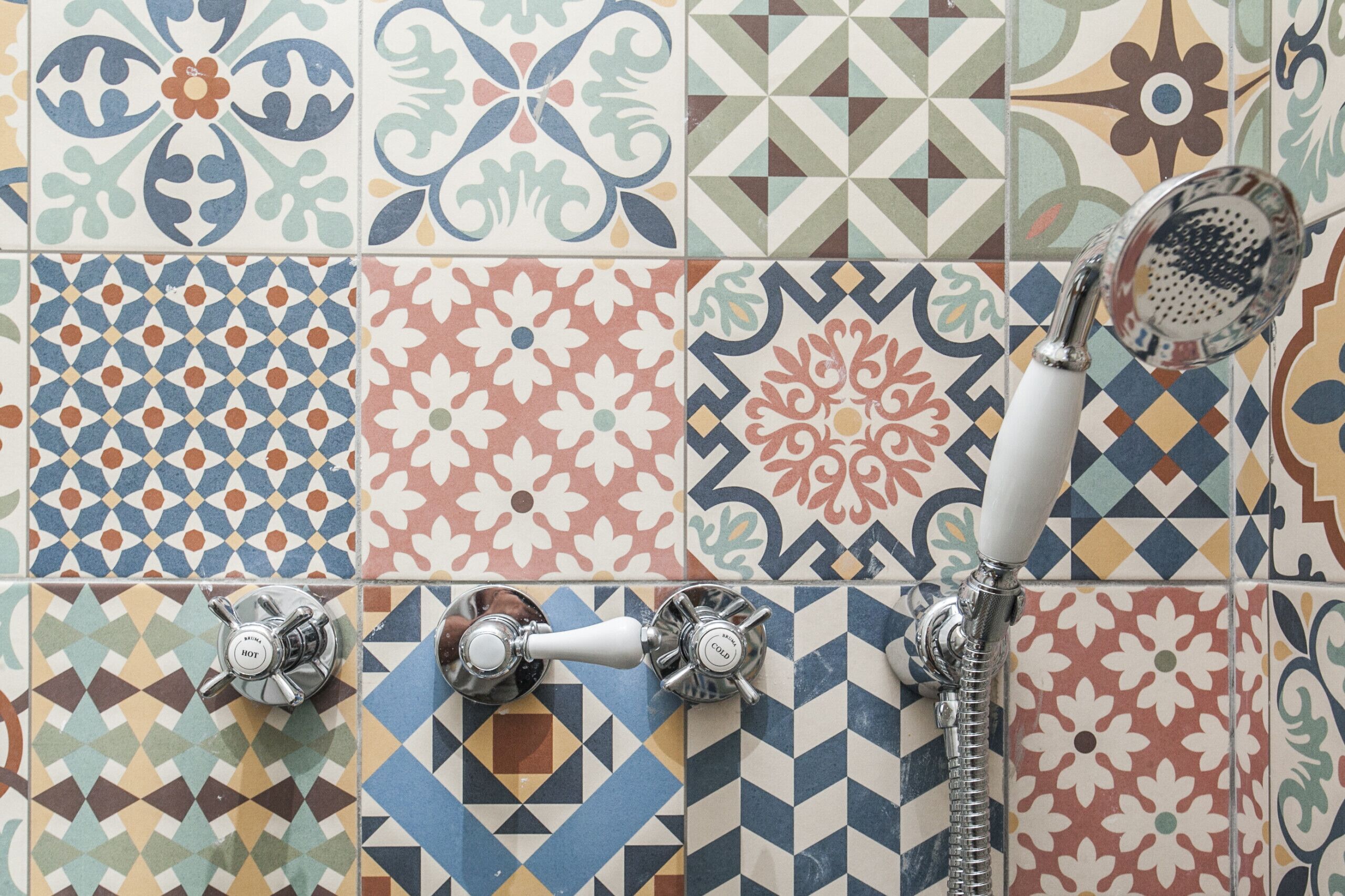 Une salle de bain avec une variété de carreaux aux motifs différents et deux robinets de douche chromés.