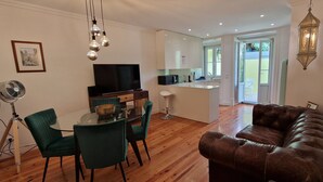 A modern living room with a brown leather sofa, a dining table with chairs, a TV, and a kitchen area visible through an open door. - Pateo Boaventura in Bairro Alto (Lisbon)