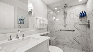 Une salle de bain moderne avec une douche en marbre, des toilettes blanches et un meuble-lavabo doté d’un grand miroir.