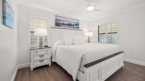 Une chambre à coucher avec un lit, des tables de chevet, un ventilateur de plafond et des œuvres d’art accrochées aux murs.