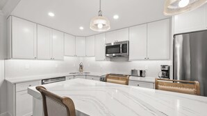 Une cuisine moderne avec des meubles blancs, un îlot en marbre et des appareils électroménagers en acier inoxydable.