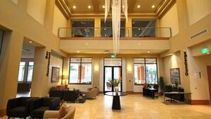 Een ruime lobby met een hoge plafond, een kroonluchter en een balkon. Er zijn zitgedeeltes en een receptiebalie.
