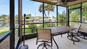 Ein überdachter Essbereich im Freien mit Tisch und Stühlen, große Fenster mit Blick auf einen See und umliegendes Grün.