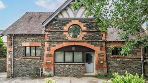 Un bâtiment en pierre avec un toit à pignon, une fenêtre circulaire et une porte.