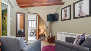 Een woonkamer met twee grijze fauteuils, een witte radiator, een aan de muur bevestigde televisie en kunstwerken in lijsten.