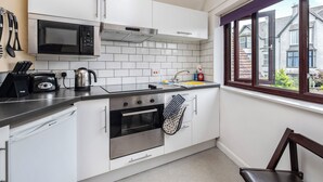 Een moderne keuken met witte kasten, een magnetron, een waterkoker en een oven.