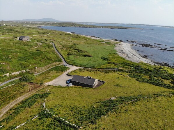 An aerial view of a coastal property with a main building, a secondary structure, and a road leading to the beach.