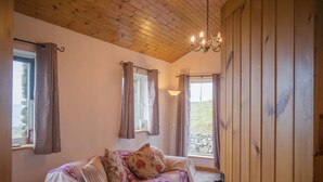 A cozy room with a wooden ceiling, a bed with floral bedding, and a view of a stone wall outside.