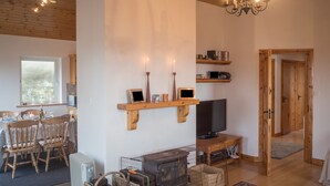 A cozy living room with a wooden ceiling, a television, a fireplace, and a dining area with chairs and a table.