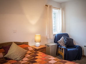 Une chambre à coucher avec un lit, une table de chevet avec une lampe, une chaise et une fenêtre avec des rideaux.