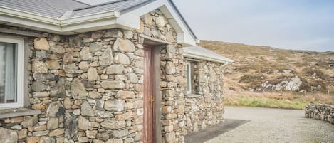 Ein Steinhaus mit roter Tür, einem Fenster und einer Steinsitzbank davor.