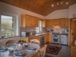 Una cocina con alacenas de madera, una mesa de comedor con platos y vasos, y una ventana con vista a la vegetación.
