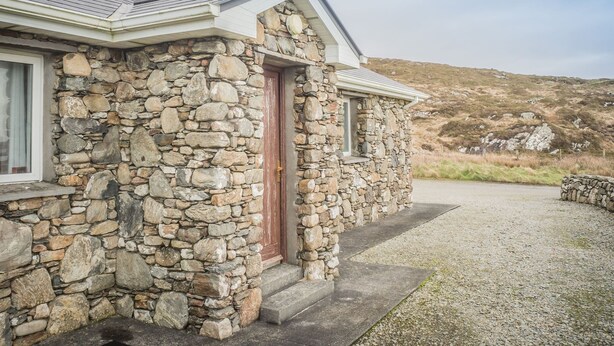 A stone house with a red door, a window, and a gravel driveway.