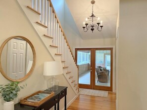 Stunning interior space with a staircase, chandelier, and large sliding glass door leading to a balcony with outdoor seating.
