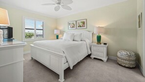 A bedroom with a white bed, bedside tables, a ceiling fan, and a window with blinds. - Waterfront Dock View 2 bed, 2 bath at Sanibel Moorings #1332 (Sanibel)
