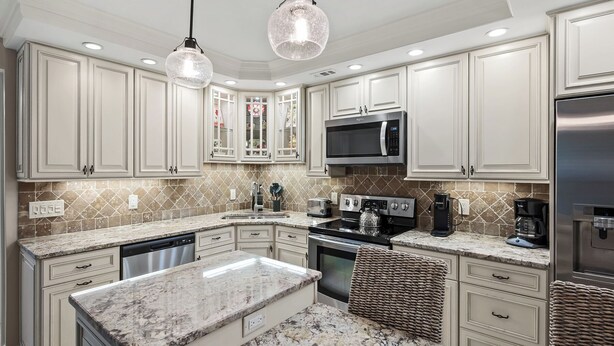 A kitchen with white cabinetry, a granite countertop, a stainless steel refrigerator, and a built-in microwave. - Waterfront Dock View 2 bed, 2 bath at Sanibel Moorings #1332 (Sanibel)