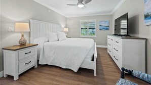Une chambre à coucher comprenant un lit, des tables de chevet, une commode, un téléviseur et un ventilateur de plafond.