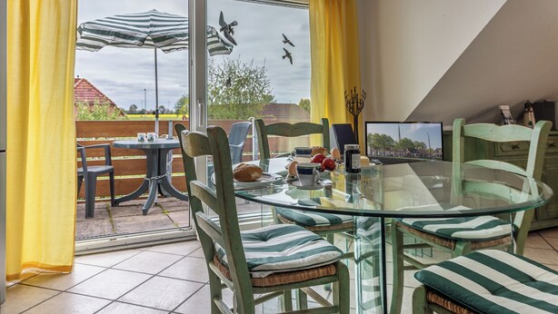 Zona pranzo con tavolo in vetro, sedie imbottite a righe e vista sul cielo attraverso una porta vetrata.